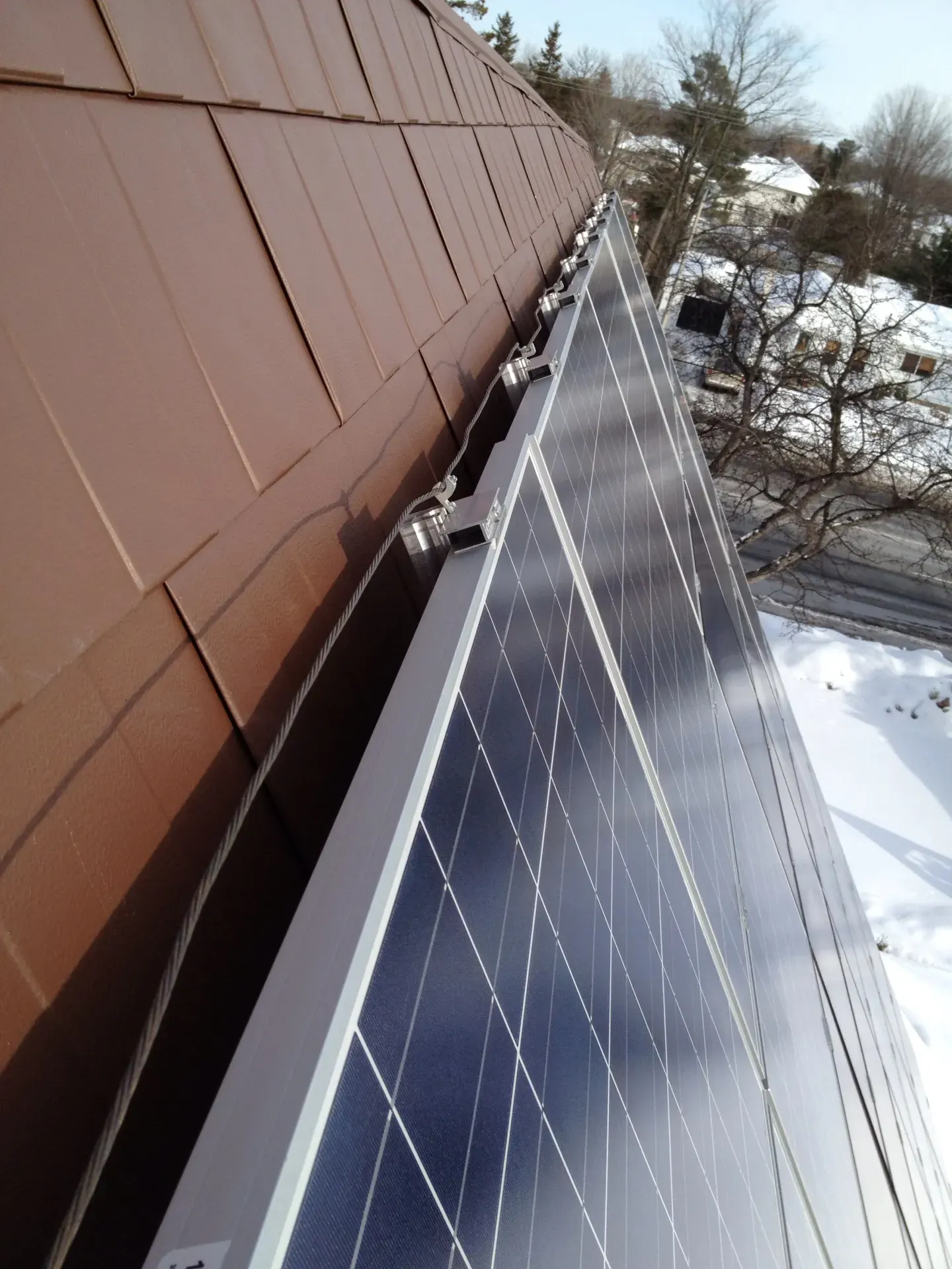A close-up of solar panels mounted on a tiled roof above a snowy yard